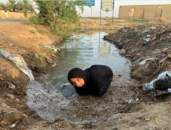 زن خوزستانی در حال تلاش برای باز کردن راه آب